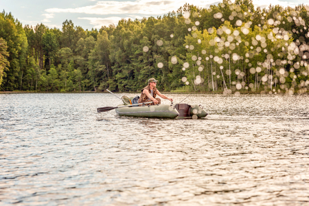 Fisherman with fishing rods is fishing in a rubber boat against background of beautiful nature and lake or river. Camping tourism relax trip active lifestyle adventure conceptの写真素材