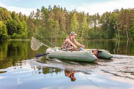 Fisherman with fishing rods is fishing in a rubber boat against background of beautiful nature and lake or river. Camping tourism relax trip active lifestyle adventure conceptの写真素材