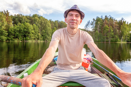 Fisherman with fishing rods is fishing in a wooden boat against background of beautiful nature and lake or river. Camping tourism relax trip active lifestyle adventure conceptの写真素材