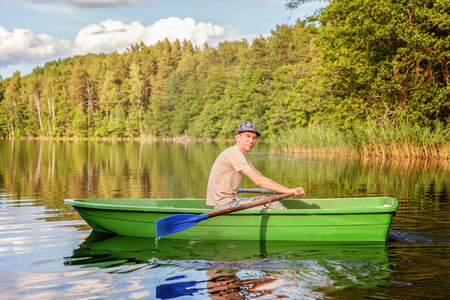 Fisherman with fishing rods is fishing in a wooden boat against background of beautiful nature and lake or river. Camping tourism relax trip active lifestyle adventure conceptの写真素材