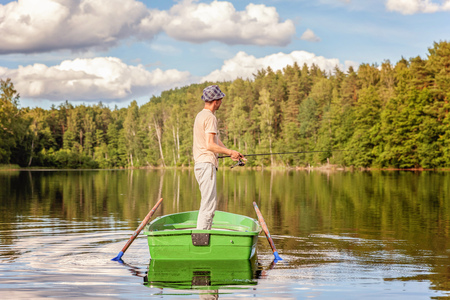 Fisherman with fishing rods is fishing in a wooden boat against background of beautiful nature and lake or river. Camping tourism relax trip active lifestyle adventure conceptの写真素材