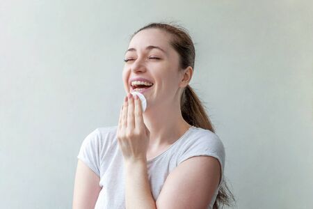 Beauty portrait of a smiling brunette woman with soft healthy skin removing make up with cotton pad isolated over white background. Skincare cleansing spa relax conceptの写真素材