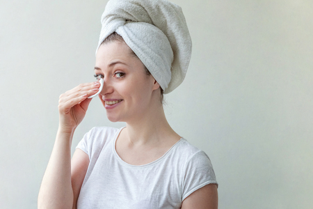 Beauty portrait of a smiling brunette woman with towel on head with soft healthy skin removing make up with cotton pad isolated over white background. Skincare cleansing spa relax conceptの写真素材