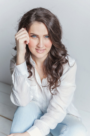 Happy teenage girl smiling. Young happy positive woman in white shirt sitting on floor in bright room against white wall. European woman. Positive human emotion facial expression body languageの写真素材