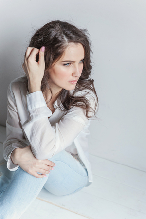 Happy teenage girl smiling. Young happy positive woman in white shirt sitting on floor in bright room against white wall. European woman. Positive human emotion facial expression body languageの写真素材