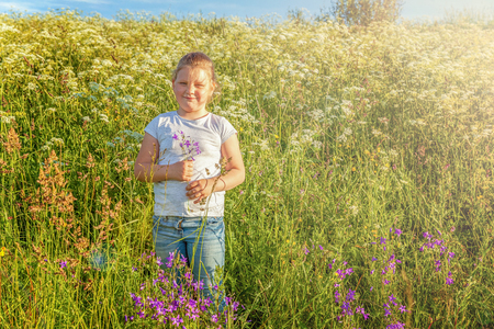 Happy cute little girl stands with a bouquet of wildflowers in the park and smiles. Happiness. Healthy preschool children summer activity. Kids playing outdoorsの写真素材