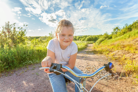 Happy child riding bike. Young girl on bicycle in sunny summer park. Healthy school children summer activity. Kids playing and cycling outdoors. Little girl learns to keep balance while riding bicycleの写真素材