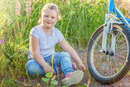 Happy child sitting near bike. Young little girl with bicycle in sunny summer park. Healthy school children summer activity. Kids playing and cycling outdoorsの写真素材