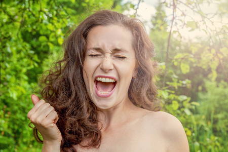 Beautiful young girl smiling and screaming on park background. European woman. Winning success positive human emotion, facial expression, body language, happy ecstatic celebrating being a winnerの写真素材