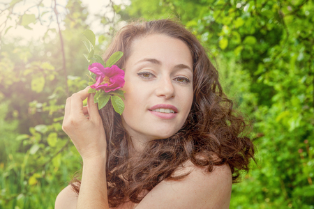Beautiful young brunette girl with perfect skin holding red rose flower in hand on park or garden green background. Beauty nature skincare eco organic cosmetic ecology pure health conceptの写真素材