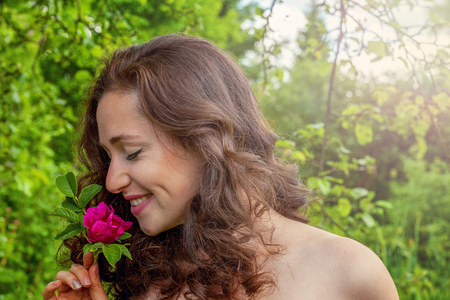 Beautiful young brunette girl with perfect skin holding red rose flower in hand on park or garden green background. Beauty nature skincare eco organic cosmetic ecology pure health conceptの写真素材