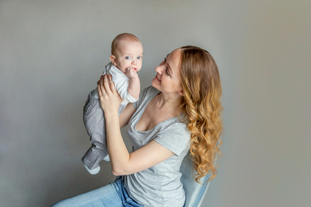 Young mother holding her newborn child. Woman and infant boy relax playing on white background. Mom of breast feeding baby. Family, maternity, tenderness, parenthood, responsibility conceptの写真素材