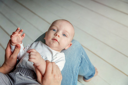 Newborn child lies on mother lap. Mom holding her infant baby boy. Woman and son relax and playing in white bright bedroom. Family, maternity, tenderness, parenthood, responsibility conceptの写真素材