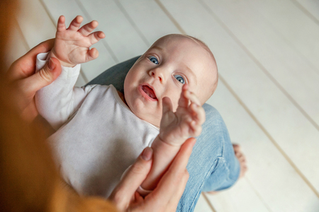 Newborn child lies on mother lap. Mom holding her infant baby boy. Woman and son relax and playing in white bright bedroom. Family, maternity, tenderness, parenthood, responsibility conceptの写真素材