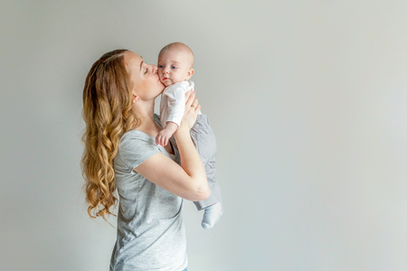 Young mother holding her newborn child. Woman and infant boy relax and playing on white background. Mom of breast feeding baby. Family, maternity, tenderness, parenthood, responsibility conceptの写真素材