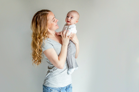 Young mother holding her newborn child. Woman and infant boy relax and playing on white background. Mom of breast feeding baby. Family, maternity, tenderness, parenthood, responsibility conceptの写真素材