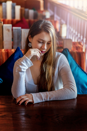Beautiful teenage young smiling brunette girl sitting in cafe or bar at table. Woman in restaurant waiting cup of coffee. Rest, enjoy, leisure, relaxation, coffee break, good morning conceptの写真素材