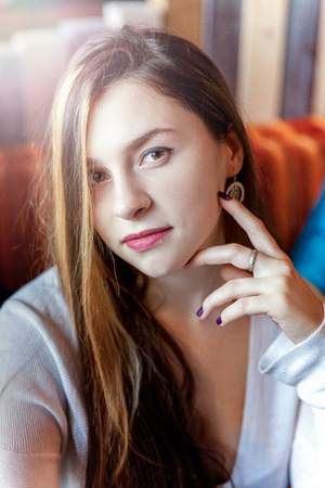 Beautiful teenage young smiling brunette girl sitting in cafe or bar at table. Woman in restaurant waiting cup of coffee. Rest, enjoy, leisure, relaxation, coffee break, good morning conceptの写真素材