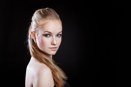Beauty fashion model girl with long healthy smooth straight hair ponytail hairstyle on black background. Smiling pretty woman looking camera. Perfect Fresh Skin Portrait. Youth and Skin Care Conceptの写真素材