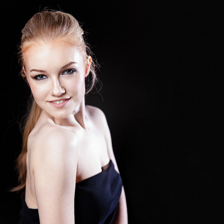 Beauty fashion model girl with long healthy smooth straight hair ponytail hairstyle on black background. Smiling pretty woman looking camera. Perfect Fresh Skin Portrait. Youth and Skin Care Conceptの写真素材