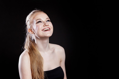 Beauty fashion model girl with long healthy smooth straight hair ponytail hairstyle on black background. Smiling pretty woman looking camera. Perfect Fresh Skin Portrait. Youth and Skin Care Conceptの写真素材