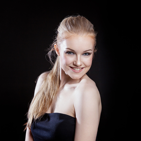 Beauty fashion model girl with long healthy smooth straight hair ponytail hairstyle on black background. Smiling pretty woman looking camera. Perfect Fresh Skin Portrait. Youth and Skin Care Conceptの写真素材