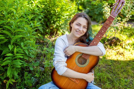Young hipster woman sitting in grass and playing guitar on park or garden background. Teen girl learning to play song and writing music. Hobby, lifestyle, relax, Instrument, leisure, education conceptの写真素材