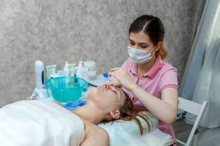 Close-up of young beauty brunette woman getting face treatment with white nourishing creme in spa salon. Face massage. Spa skin and body care. Skincare cleansing cosmetic spa relax conceptの写真素材