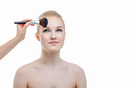 Hand of makeup master applying powder for young woman model on white background. Professional make up applying by artist. Beautiful girl face with perfect skin. Make-up detail in processの写真素材