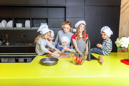 Happy family in kitchen. Mother and five children preparing dough, bake apple pie. Mom, daughters and sons cooking healthy food at home and having fun. Household, teamwork helping, maternity conceptの写真素材