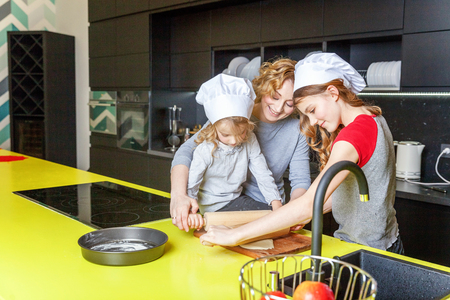 Happy family in kitchen. Mother and two children preparing dough, bake apple pie. Mom and daughters cooking healthy food at home and having fun. Household, teamwork helping, maternity conceptの写真素材