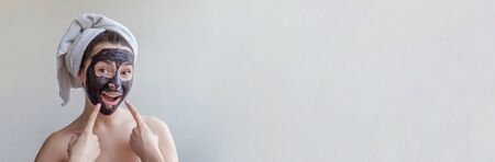 Beauty portrait of woman in towel on head applying black nourishing mask on face, white background isolated. Skincare cleansing eco organic cosmetic spa relax concept Bannerの写真素材