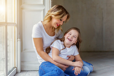 Mother hugging child. Woman and girl relax and playing in bedroom near windiow. Happy family at home. Mom playing with her daughter. Family, maternity, tenderness, parenthood, responsibility conceptの写真素材