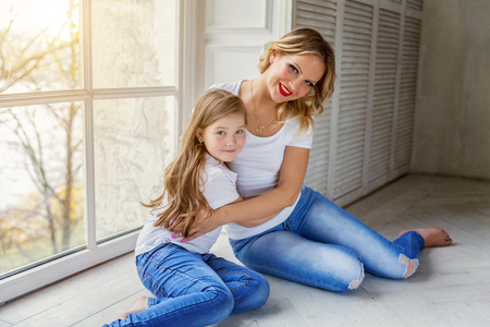 Mother hugging child. Woman and girl relax and playing in bedroom near windiow. Happy family at home. Mom playing with her daughter. Family, maternity, tenderness, parenthood, responsibility conceptの写真素材