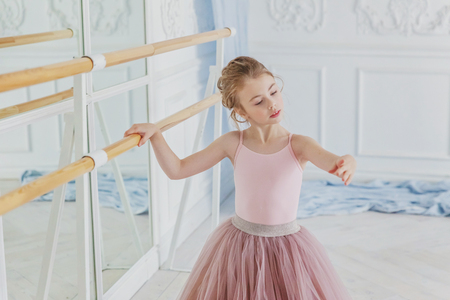 Young classical ballet dancer girl in dance class. Beautiful graceful ballerina practice ballet positions in pink tutu skirt near large mirror in white light hallの写真素材