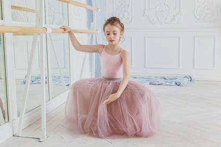 Young classical ballet dancer girl in dance class. Beautiful graceful ballerina practice ballet positions in pink tutu skirt near large mirror in white light hallの写真素材