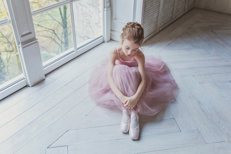 Young classical ballet dancer girl in dance class. Beautiful graceful ballerina practice ballet positions in pink tutu skirt in white light hallの写真素材