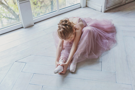 Young classical ballet dancer girl in dance class. Beautiful graceful ballerina practice ballet positions in pink tutu skirt in white light hallの写真素材