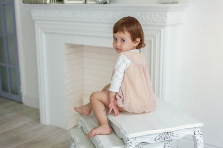 Sweet little girl in pastel pink dress at home sitting on modern cozy grey chair relaxing in white living room. Childhood, preschool, youth, relax conceptの写真素材