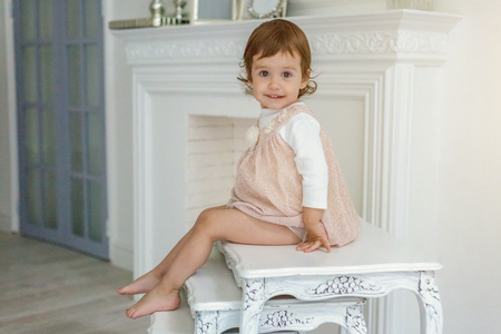 Sweet little girl in pastel pink dress at home sitting on modern cozy grey chair relaxing in white living room. Childhood, preschool, youth, relax conceptの写真素材