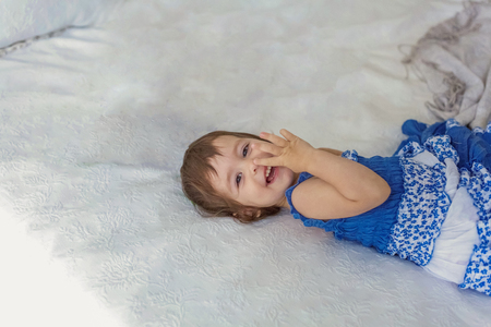 Funny and cute brunette little smiling girl playing jumping on bed in light bedroom. White interior with big bed. Childhood, preschool, youth, relax conceptの写真素材