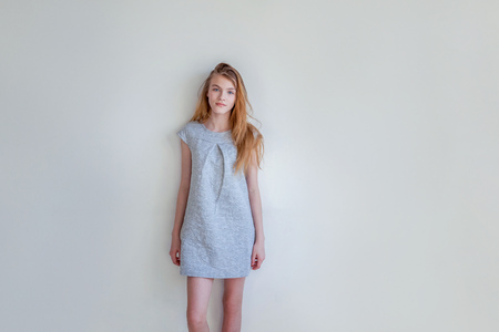 Happy teenage girl smiling. Closeup portrait young happy positive woman in grey dress at home in bright room against white wall. European woman. Positive human emotion facial expression body languageの写真素材