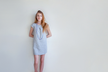 Happy teenage girl smiling. Closeup portrait young happy positive woman in grey dress at home in bright room against white wall. European woman. Positive human emotion facial expression body languageの写真素材