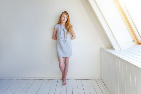 Happy teenage girl smiling. Closeup portrait young happy positive woman in grey dress at home in bright room against white wall. European woman. Positive human emotion facial expression body languageの写真素材