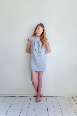 Happy teenage girl smiling. Closeup portrait young happy positive woman in grey dress at home in bright room against white wall. European woman. Positive human emotion facial expression body languageの写真素材
