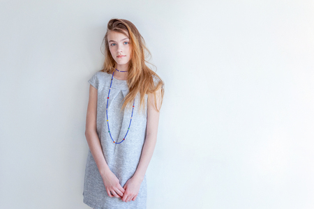 Happy teenage girl smiling. Closeup portrait young happy positive woman in grey dress at home in bright room against white wall. European woman. Positive human emotion facial expression body languageの写真素材