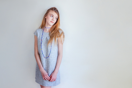 Happy teenage girl smiling. Closeup portrait young happy positive woman in grey dress at home in bright room against white wall. European woman. Positive human emotion facial expression body languageの写真素材