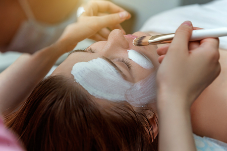 Close-up of young beauty brunette woman getting face treatment with white nourishing creme in spa salon. Face massage. Spa skin and body care. Skincare cleansing cosmetic spa relax conceptの写真素材