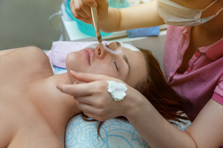 Close-up of young beauty brunette woman getting face treatment with white nourishing creme in spa salon. Face massage. Spa skin and body care. Skincare cleansing cosmetic spa relax conceptの写真素材
