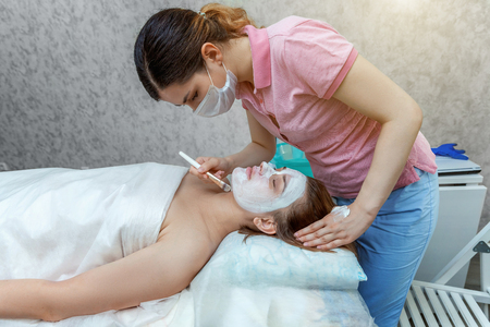 Close-up of young beauty brunette woman getting face treatment with white nourishing creme in spa salon. Face massage. Spa skin and body care. Skincare cleansing cosmetic spa relax conceptの写真素材